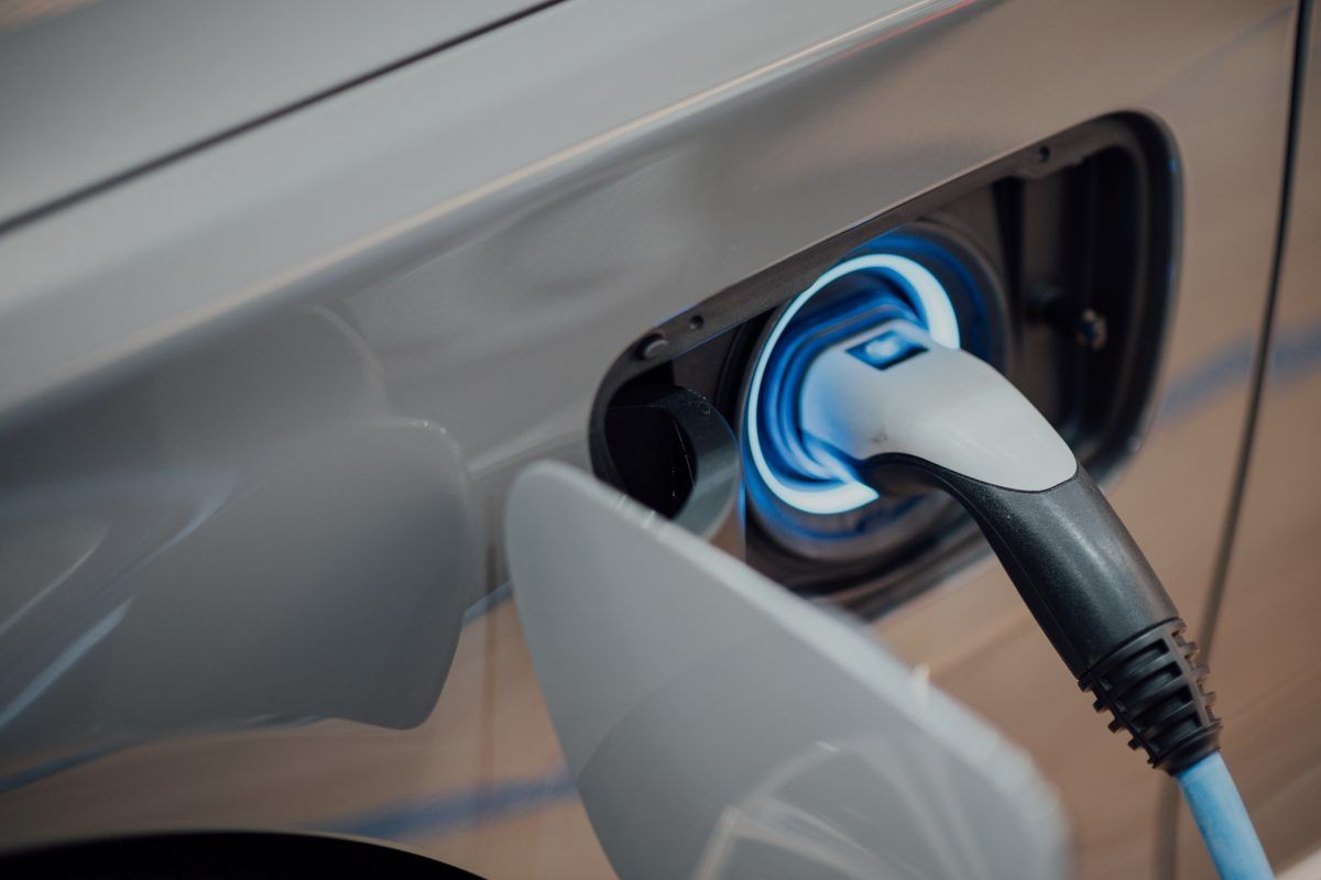 Close-up of an electric car charging port with a plugged-in charger emitting blue light.