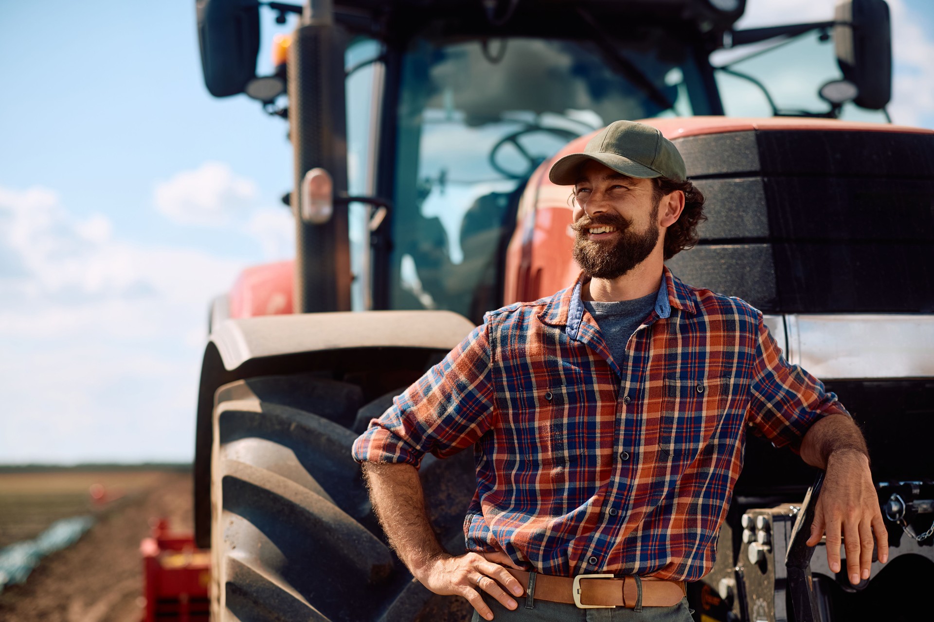 Happy farm worker leaning on a tractor and looking away.